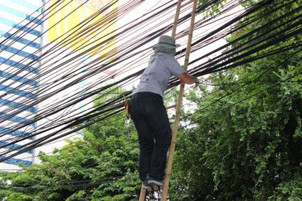 Un operario repara el tendido eléctrico, sujetado por una escalera de bambú, en plena calle de Bangkok.